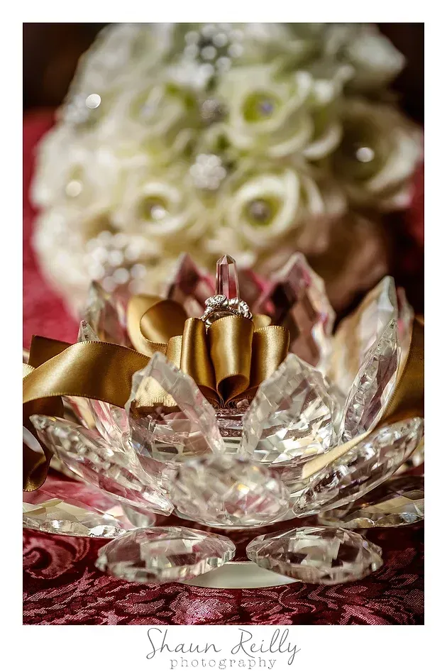Crystal lotus candle holder with gold petals, set before a blurred white floral bouquet.