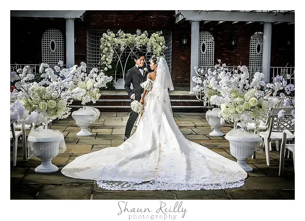 Bride and groom standing in a floral wedding venue, with the bride in a long white gown and veil