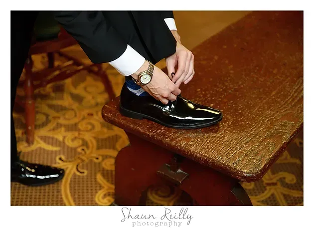 Person polishing a black dress shoe on a wooden shoe shine stand in a patterned room.