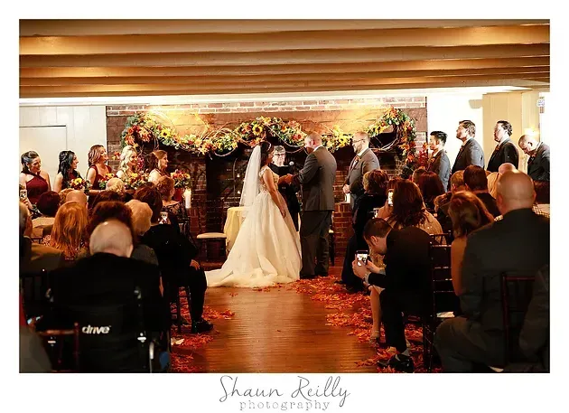 Wedding ceremony with bride in white gown at altar, guests seated on both sides in warm indoor venue