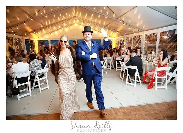 Two wedding guests in formal attire posing inside a warmly lit reception tent