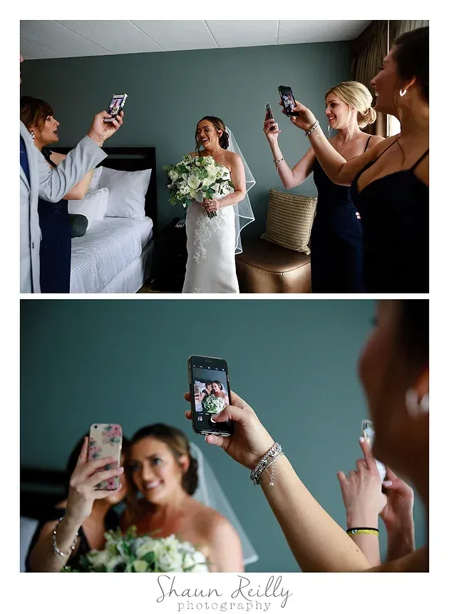 Bride posing for photos while guests film her on phones in a hotel room