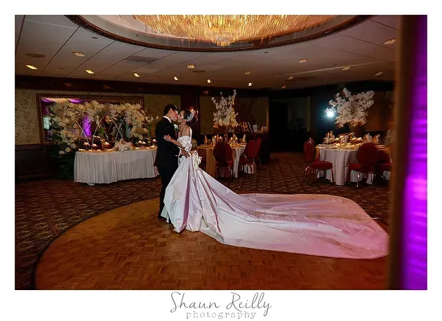 Bride and groom dancing in a ballroom, with the bride’s long white train flowing behind them