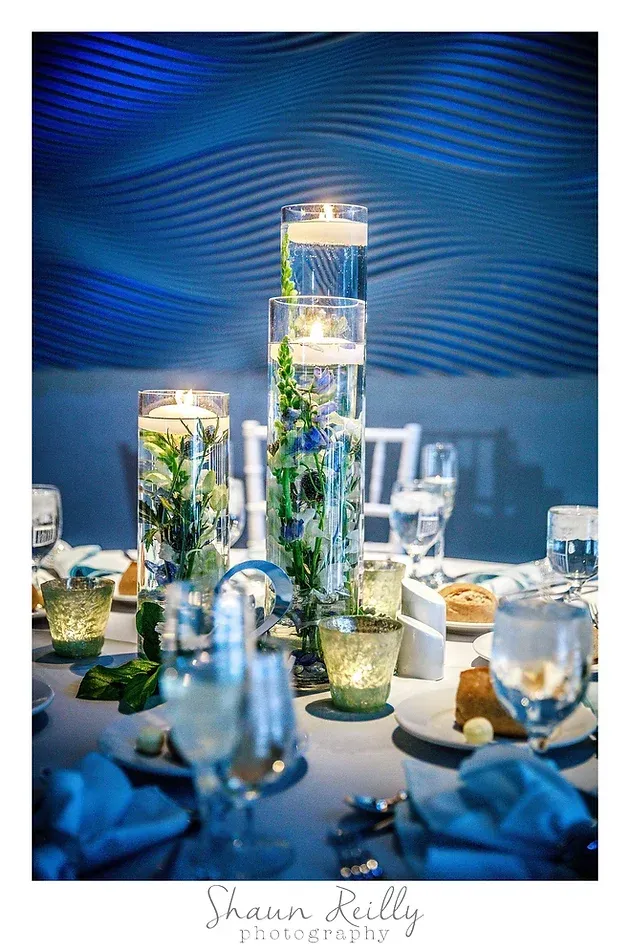Blue-lit candle centerpiece with floating flowers and glass vases on a decorated table
