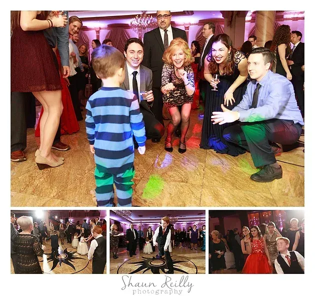 Child in blue striped outfit approaches seated adults at a lively party with dancing and purple lighting.