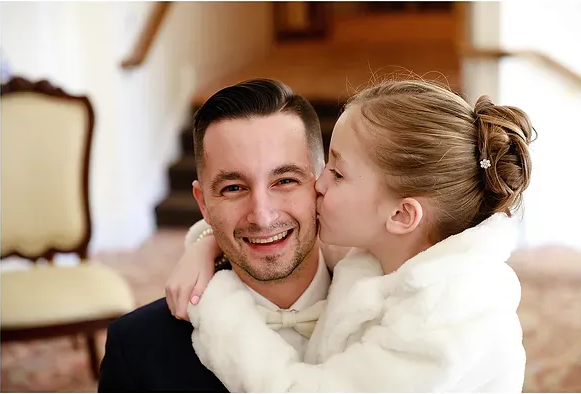 Smiling man with a child in a white coat hugging and kissing his cheek indoors
