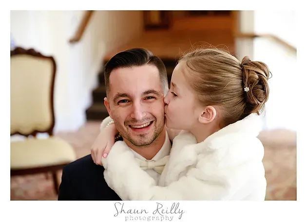 Smiling couple in a warm indoor setting, woman kissing man on the cheek while hugging him