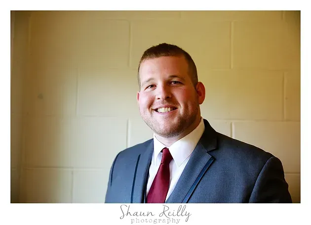 Smiling man in a gray suit and red tie against a beige wall