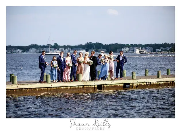 Wedding party posing on a dock by the water, with bride and groom in the center.