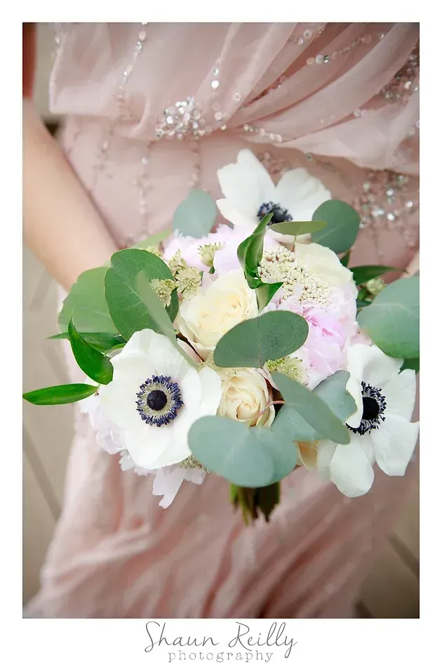 Bride holding a bouquet of white and blush flowers with eucalyptus leaves against a pink dress