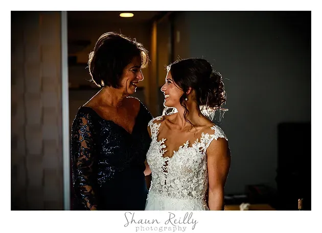 Two brides in white and navy dresses smiling at each other in a dimly lit room