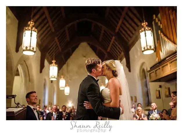 Bride and groom kiss at the altar in a warmly lit church wedding ceremony.