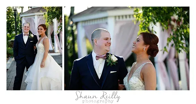 Wedding couple posing outdoors in formal attire beside a pink building, smiling in a garden setting