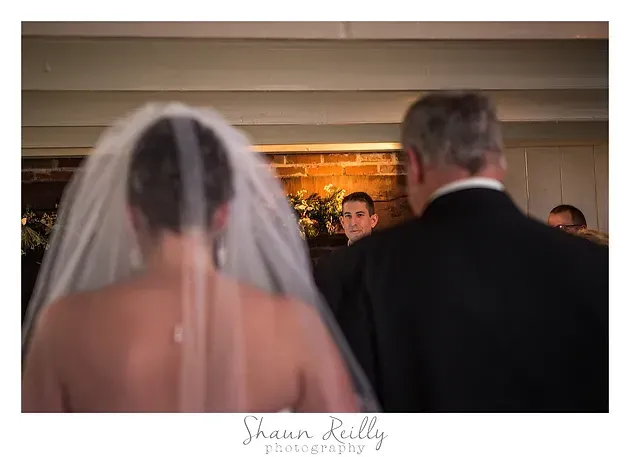 Bride seen from behind walking toward groom in a church aisle during wedding ceremony