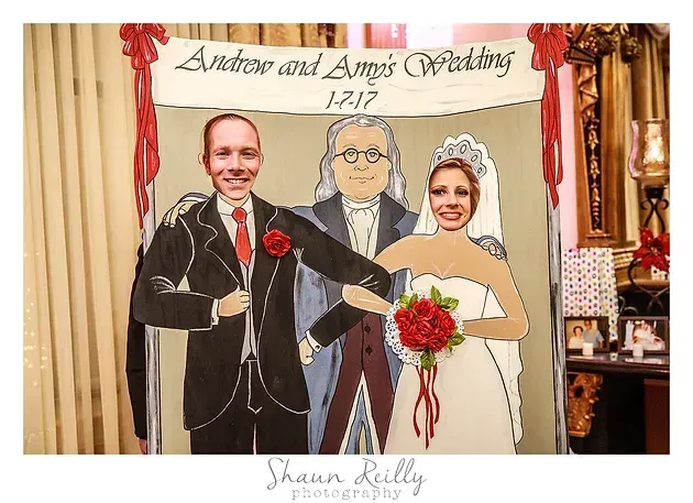 Cartoon wedding cutout of a bride and groom holding flowers at a reception display, with a hand-painted minister between them