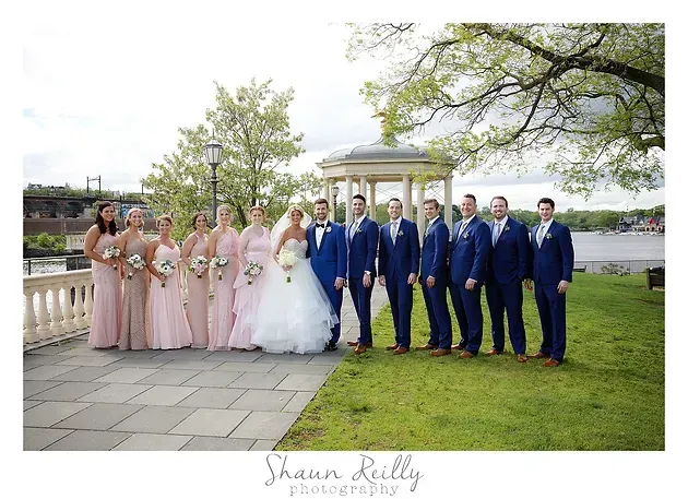 Wedding party posing outdoors by a river, bride in white, bridesmaids in blush, groomsmen in blue suits