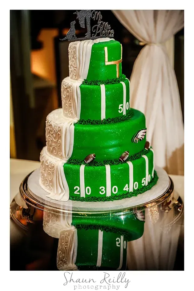 Green tiered wedding cake with white accents and white clock-like numbers on a reflective table