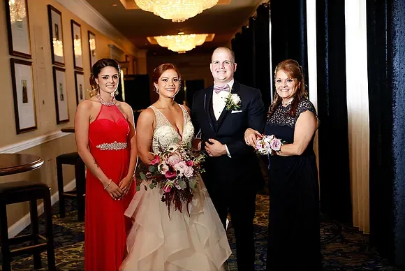 Four people posing in formal attire at a wedding reception, holding bouquets and smiling.