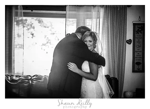 Black-and-white photo of a couple embracing indoors by a curtained window