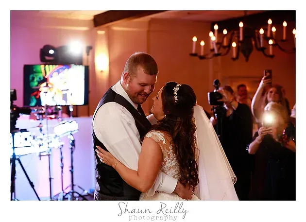 Bride and groom dancing at a warmly lit wedding reception with guests and candle chandeliers nearby