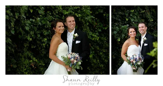 Bride and groom pose together in wedding attire before a leafy green backdrop.