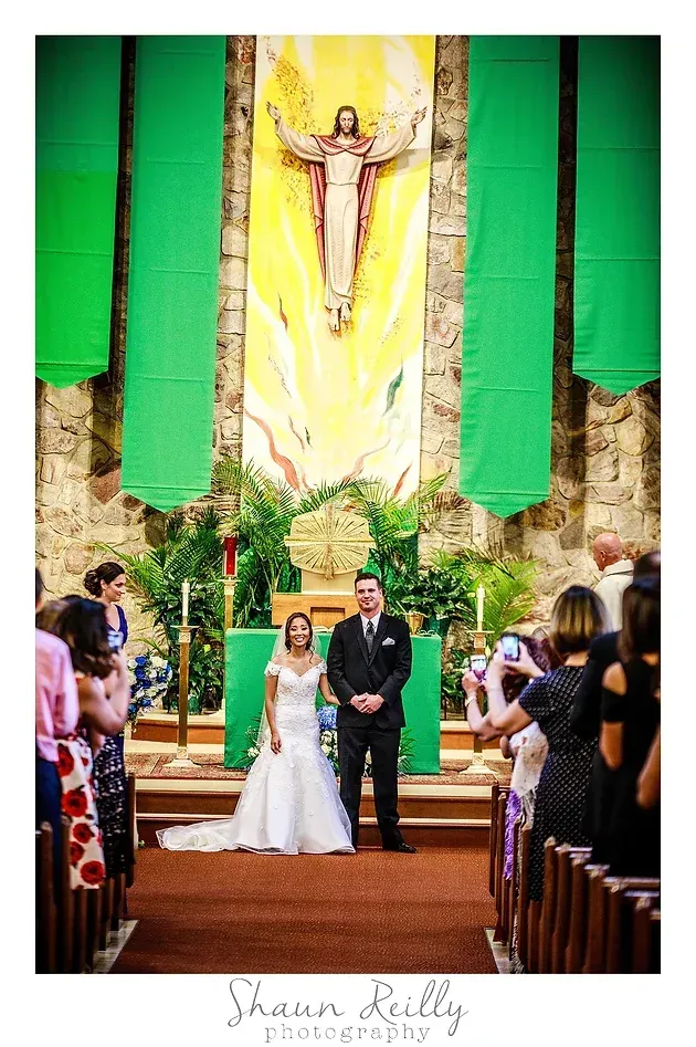 Bride and groom at the altar in a church, framed by green drapes and a large statue above them