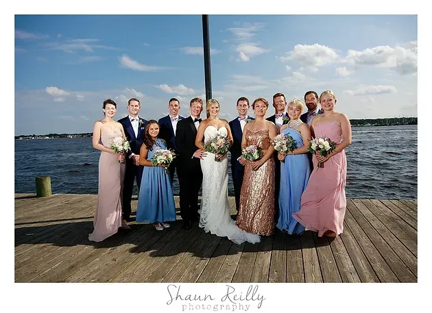 Wedding party posing on a dock by the water, with the bride in white and bridesmaids in pastel dresses