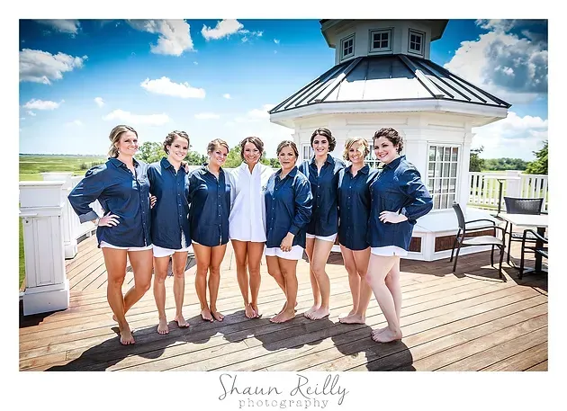 Seven people in navy robes on a bright rooftop deck by a white gazebo, posing for a group photo