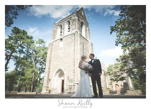 Bride and groom posing beside a stone church tower under a blue sky