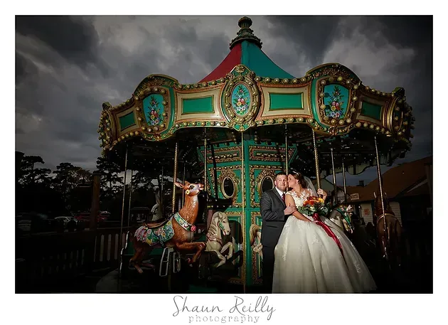 Bride on a carousel horse at night, with a teal and gold carousel in the background.