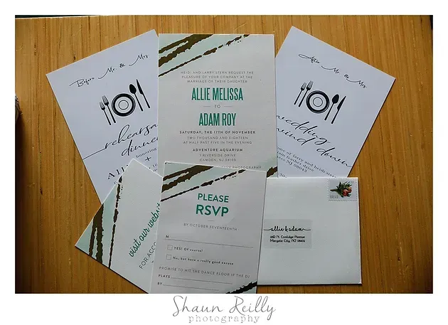 Wedding invitation suite on wooden table, with white and mint-green cards and RSVP envelope.