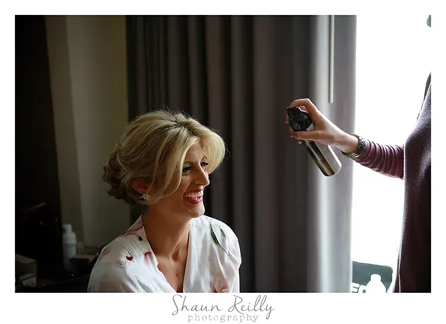 Woman in a robe getting her hair styled by a hand-held spray tool near a window