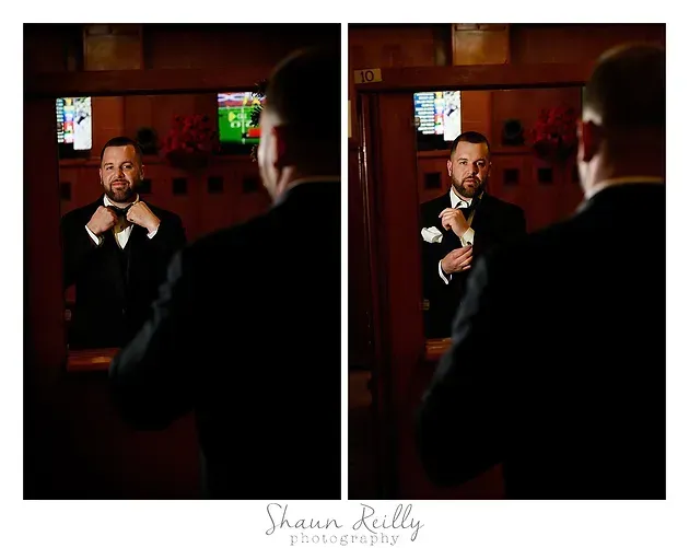 Man in a tuxedo adjusting his bow tie in a dimly lit bar, seen in a mirror reflection.