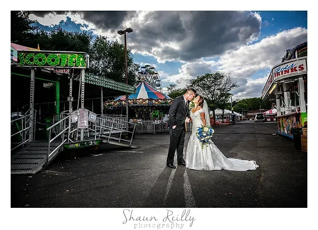 Bride and groom in wedding attire posing in an empty amusement park under cloudy skies