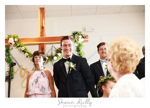 Wedding couple standing at altar with floral cross and smiling guests in church