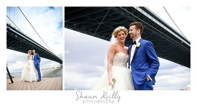 Bride and groom posing under a bridge, with blue sky and waterfront walkway in the background
