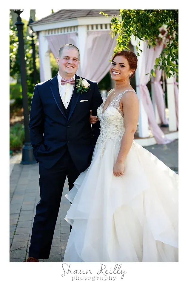 Bride and groom posing outdoors in a garden wedding setting, smiling at the camera