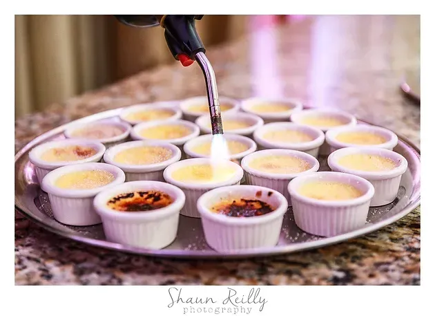 Flame-torched custard cups arranged on a tray, with a caramelized topping being added to one dessert