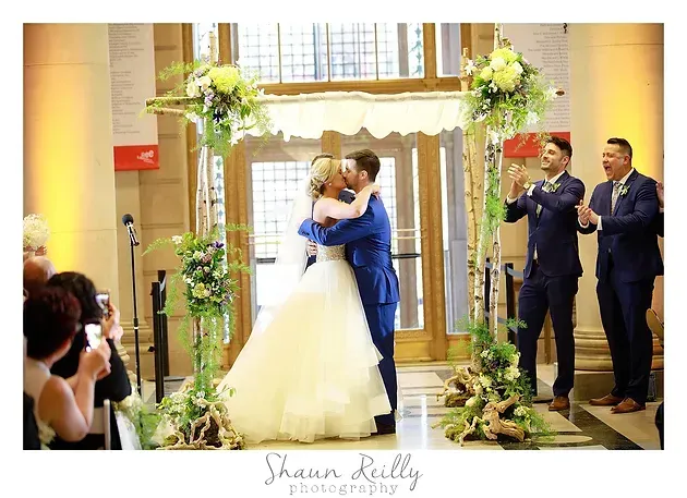 Bride and groom embrace at the altar as guests applaud in a warmly lit wedding venue