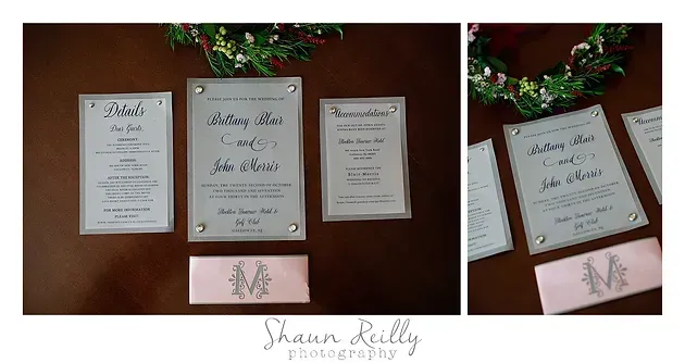 Three framed wedding ceremony printouts on a table, with a small pink box and floral greenery above.