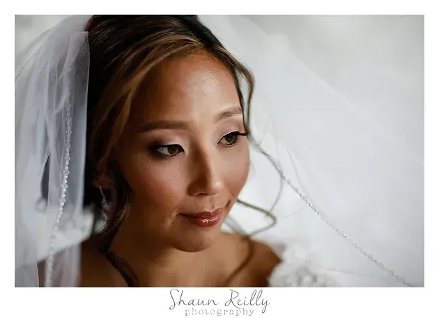 Bride in a white veil looking down with a soft smile, in a bright close-up portrait