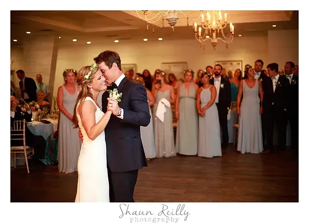 Bride and groom sharing a first dance at their wedding reception, with guests watching nearby.