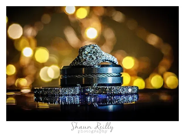 Two silver rings with a diamond on a reflective surface, with warm golden bokeh lights in the background