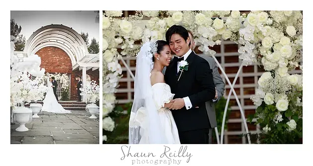 Wedding couple under white floral arch, embracing on steps beside an ornate brick doorway