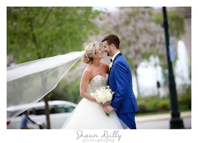 Bride and groom kissing outdoors, bride’s veil flowing in the wind
