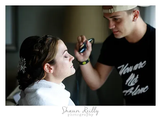 Man applying makeup to seated woman in a softly lit room