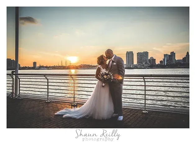 Couple embracing by a waterfront at sunset with city skyline in the background