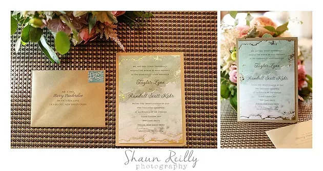 Three wedding invitation cards displayed on a woven mat with greenery and flowers.