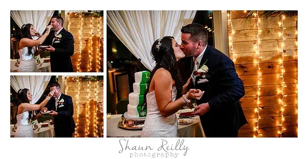 Wedding couple kissing beside a tiered cake, with warm string lights and draped curtains in the background