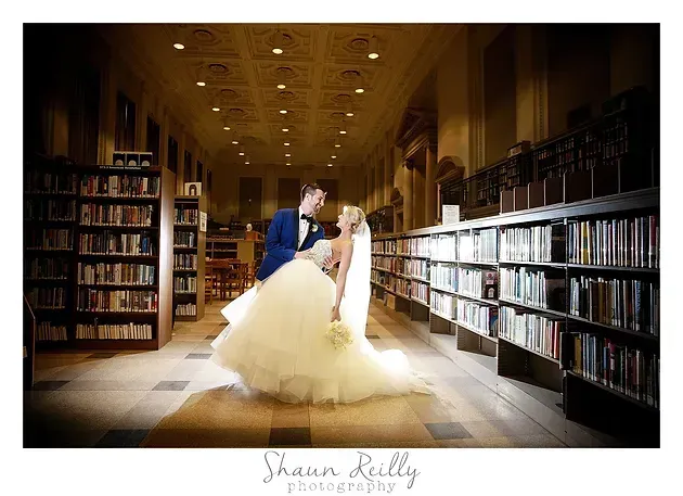 Bride and groom embrace in a warm-lit library aisle